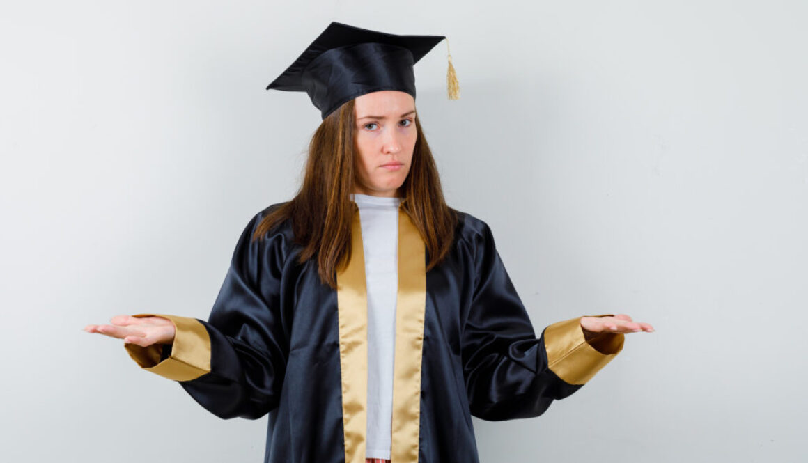 young female graduate in academic dress showing helpless gesture and looking indecisive , front view.